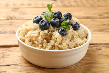 Tasty quinoa porridge with blueberries and mint in bowl on wooden table, closeup