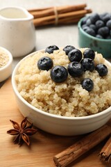 Tasty quinoa porridge with blueberries in bowl and spices on table, closeup