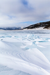 Winter landscape of frozen Baikal Lake on a cold February day. Tourists come to the lake shore by car to skate and walk on the ice. Natural background. Winter ice travel and outdoor recreation