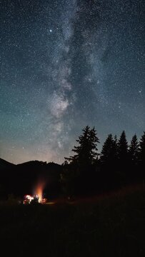 Vertical video of Friends sitting by campfire under starry night sky with milky way galaxy stars over forest nature Time lapse Outdoor adventure social media story