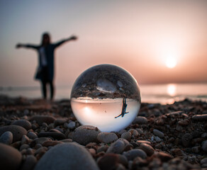 Reflection of a happy woman on the beach at sunset inside a crystal ball