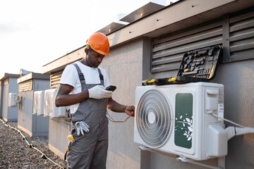 Busy civil engineer dressed in gray jumpsuit holding digital multimeter and checking voltage level...