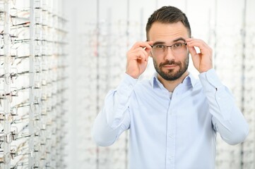 Healthcare, Eyesight And Vision Concept. Happy man choosing glasses at optics store, selective focus