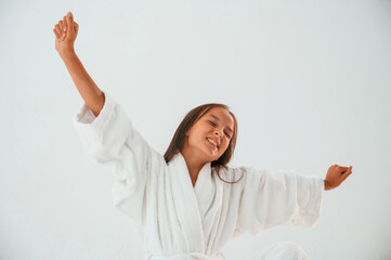 Young female kid is standing against white background