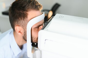 Handsome young man is checking the eye vision in modern ophthalmology clinic. Patient in...