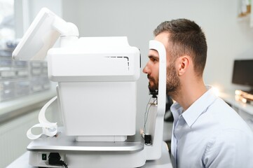 Handsome young man is checking the eye vision in modern ophthalmology clinic. Patient in...