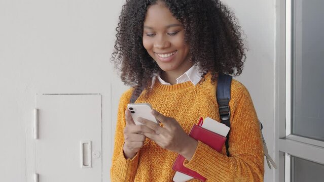 Black women with short, curly hair looks at the flight schedule on smartphone in an airport to check the gate and time to board the plane to travel or study abroad.