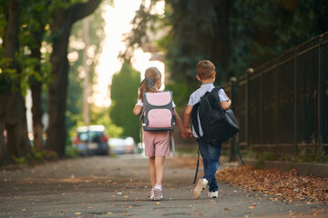 Back view, walking. Young school children of boy and girl are together outdoors