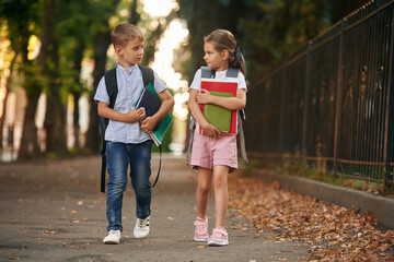 Holding notebook and books. Young school children of boy and girl are together outdoors
