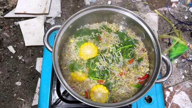A young man cooking Sayur bening bayam, Spinach Clear Vegetable. Indonesian food of spinach, spinach soup with corn