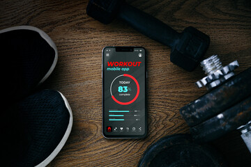 Training application on mobile phone screen. Top view of fitness dumbbells, sneakers and a...