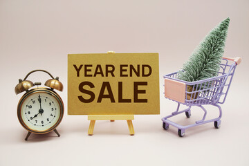 Year end sale text message with wooden easel and alarm clcok, christmas tree on trolley shopping cart on pink background
