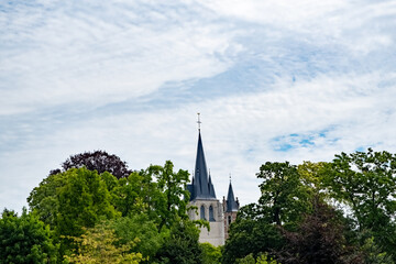 Fototapeta na wymiar This image captures the majestic spire of a church in Mechelen, gracefully piercing the sky. The church tower, with its Gothic architectural elements, stands as a silent guardian over the lush green