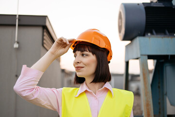 Front view of smiling female manager wearing reflective yellow vest standing near construction...