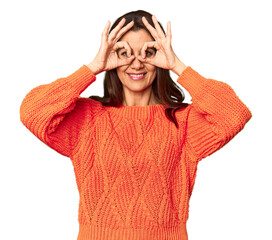 Elegant middle-aged Caucasian woman in studio setting showing okay sign over eyes