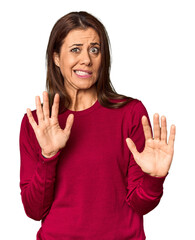 Elegant middle-aged Caucasian woman in studio setting rejecting someone showing a gesture of...