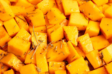 Close up shot of diced pumpkin pieces in a bowl, with spices and olive oil, viewed from above