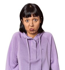 Young Hispanic woman with short black hair in studio shrugs shoulders and open eyes confused.