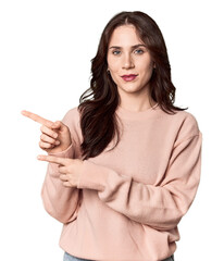 Young Caucasian woman in a studio setting excited pointing with forefingers away.