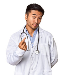 Young Chinese man as a medical doctor in studio pointing with finger at you as if inviting come closer.