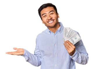 Young Chinese man holding dollar bills in studio showing a copy space on a palm and holding another hand on waist.