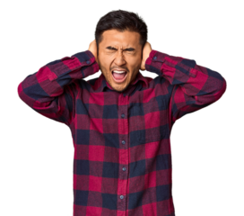 Young Chinese man in studio background covering ears with hands trying not to hear too loud sound.