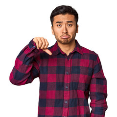 Young Chinese man in studio background showing a dislike gesture, thumbs down. Disagreement concept.