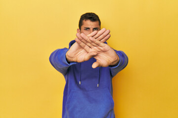 Young Hispanic man on yellow background doing a denial gesture