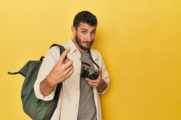 Young Hispanic travel photographer poses pointing with finger at you as if inviting come closer.