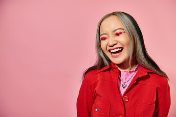 Valentines day concept, happy asian woman with heart eye makeup laughing on pink background