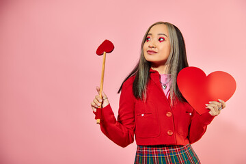Valentines day, happy asian girl with vibrant eye makeup holding carton heart on pink backdrop