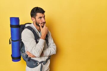 Young Hispanic man ready for hiking looking sideways with doubtful and skeptical expression.