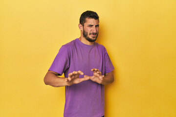 Young Hispanic man on yellow background rejecting someone showing a gesture of disgust.