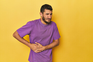 Young Hispanic man on yellow background having a liver pain, stomach ache.