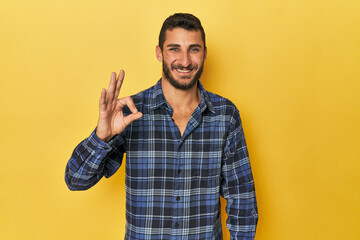Young Hispanic man on yellow background cheerful and confident showing ok gesture.