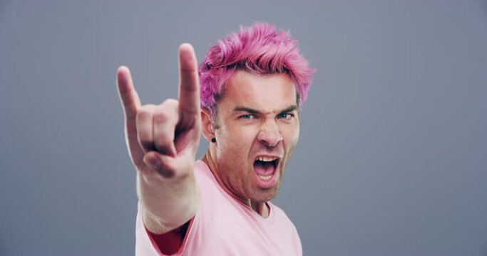 Rock hand gesture, tongue out or face of man in studio on grey background for freedom or wild energy Pink hair, crazy or portrait of cool person isolated for devil horns sign, punk or edgy attitude