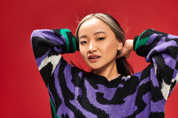 pretty and young asian woman with dyed hair in vibrant sweater with animal print posing on red