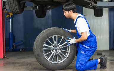 Fototapeta na wymiar Male mechanic wearing uniform, changing rubber tyre or tire wheel, working, repairing in the garage at car or automobile maintenance service center or shop with copy space. Industry Concept.