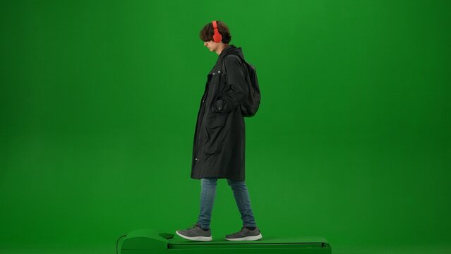 Portrait of person tourist isolated on chroma key green screen background. Young man in coat and headphones walking and listening music.