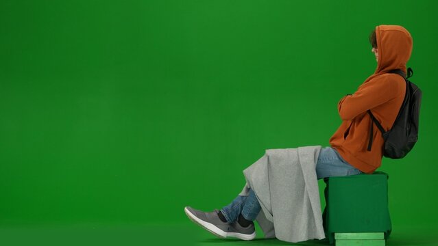 Portrait of person tourist isolated on chroma key green screen background. Young man sitting covered in plaid with hood on, taking nap waiting for flight.