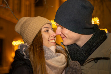 Positive, cheerful couple hugging during x-mas evening. Decorated lights on the streets outdoors