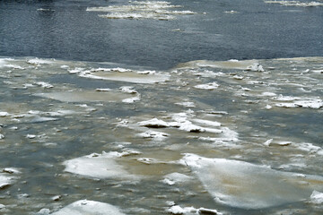 The water in the river begins to freeze in winter on a dark cloudy day.