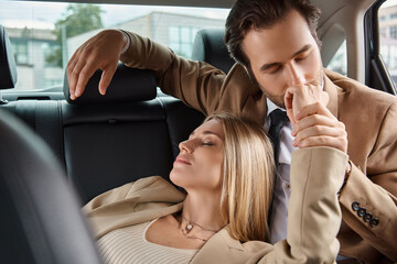 businessman in suit kissing hand of blonde passionate woman while traveling in car, seduction