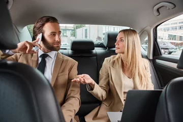 Foto op Plexiglas blonde businesswoman talking to handsome man in formal wear calling on smartphone in luxury car © LIGHTFIELD STUDIOS