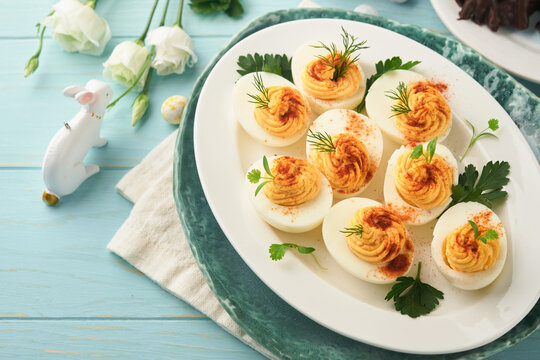 Stuffed or deviled eggs with paprika and parsley on blue plate for easter table. Traditional dish for Easter. Healthy diet food for breakfast. Top view, flat lay.