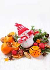 Christmas background. knitted snowman toy, fir branches, oranges decorated cloves on white wooden table. Christmas, New Year holidays concept.