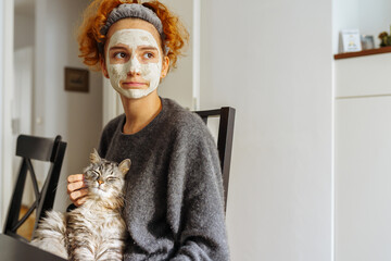 gray fluffy tabby cat sits on arms teenage girl wearing cosmetic mask