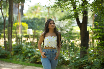 Young woman, Hispanic, beautiful, brunette, with daisy t-shirt and jeans, walking in a park, quiet and lonely. Concept of beauty, fashion, trend, nature, spring.