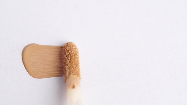A smear of foundation cream or concealer with a brush on a white background, macro. Texture of cosmetic liquid foundation or beige cream smudge, smear, stroke. Highlighter or foundation tone.
