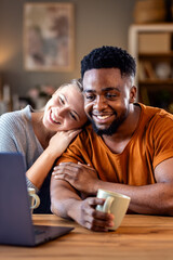Smiling young mixed couple using a laptop while working on their home finances.